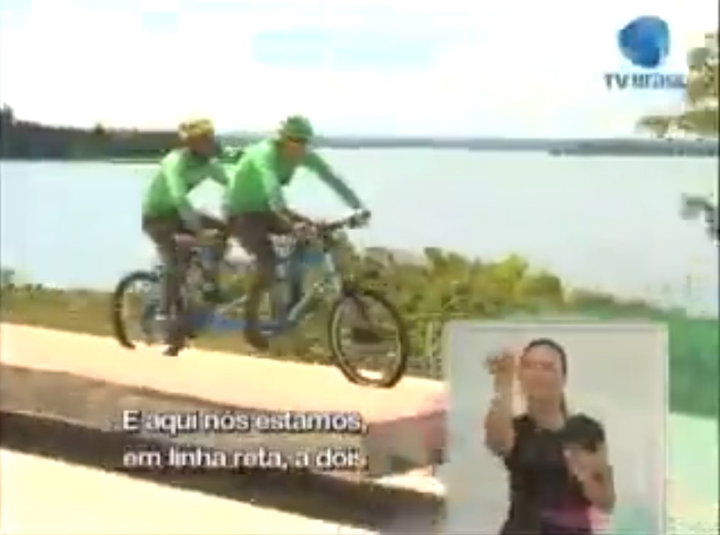 Imagem mostra Weimar e Adauto pedalando em uma praça ao lado do Lago Paranoá