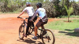 Imagem mostra uma dupla pedalando dentro do JBB, passando, de costas, com a mata por trás